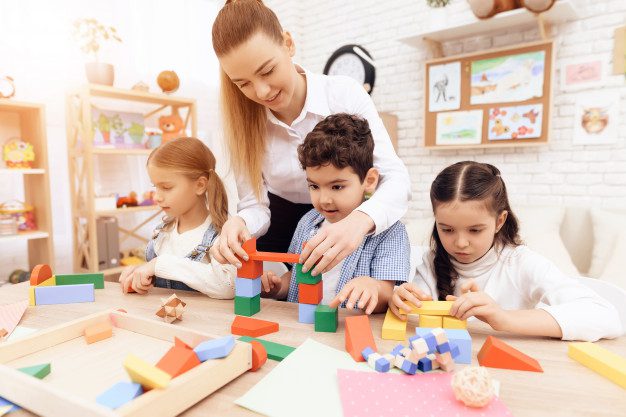 A woman and two children are playing with blocks.