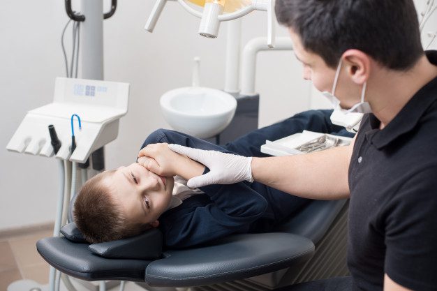 A young boy getting his teeth checked by an adult.